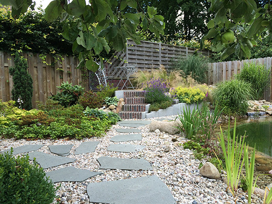 Verwunschnener Garten mit Kieselweg mit Steinplatten und Sitzecke mit Treppe